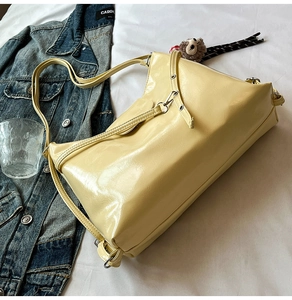 Detail of light yellow glossy PU leather tote bag with a cute plush monkey pendant