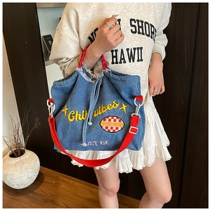 Detail of blue denim tote bag featuring yellow Chill Vibes embroidery and red strap