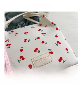 Detail van canvas emmer tas met kersenprint, lederen label en roze kwastje decoratie