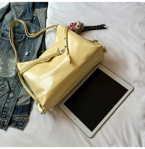 Detail view of glossy yellow patent leather tote bag with plush monkey charm on fabric