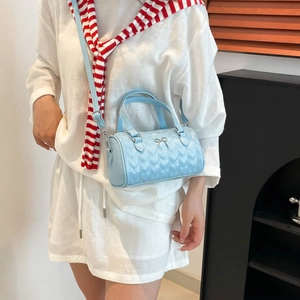 Sac cylindre bleu clair avec matelassage en cœur et nœud argenté porté par modèle