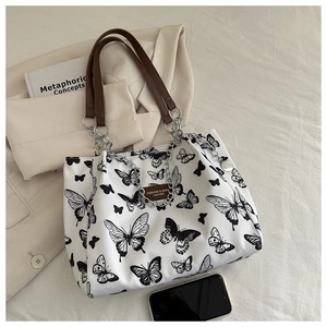 Detail of white tote bag with black butterfly print, leather handles and chain strap