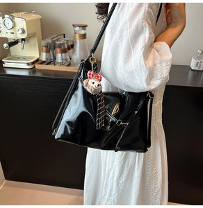 Close-up of black glossy shoulder bag with a cute bear charm and adjustable strap