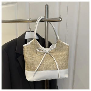 Detail of woven straw tote bag with white leather trim and decorative bow accent