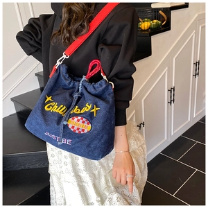 Detail of denim bucket bag with yellow embroidery and red fabric shoulder strap
