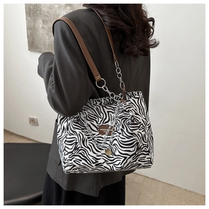 Detail of zebra-print tote bag with brown leather strap and silver chain accent