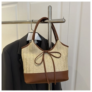 Detail of straw woven tote bag featuring brown leather trim and decorative leather bow