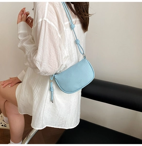 Détail d'un petit sac bandoulière bleu clair avec texture cuir grainé et bandoulière nouée