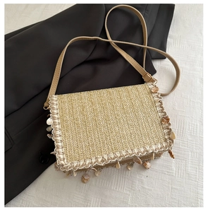 Detail of woven straw bag with decorative shell charms and adjustable leather shoulder strap