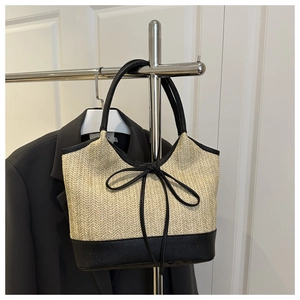 Detail of woven straw tote bag featuring black leather handles and bow decoration