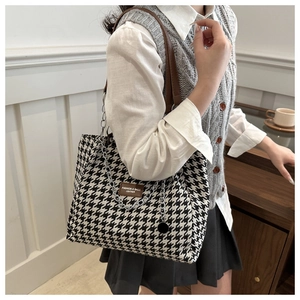 Detail of black and white houndstooth tote bag with brown leather patch and silver chain