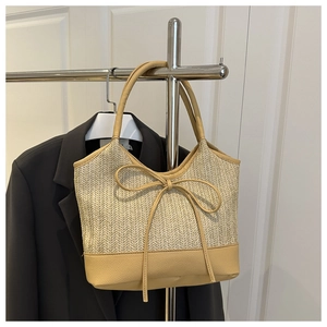 Detail of woven straw tote bag featuring a light brown faux leather bow and dual straps