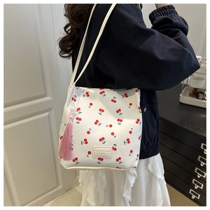 Detail van witte bucket tote bag met kersenprint en roze kwastje aan de riem