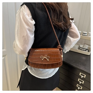 Brown crocodile embossed shoulder bag with gold bow clasp worn by a model