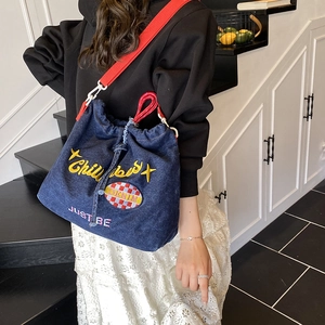 Denim drawstring bucket bag with yellow embroidery and red strap worn by a model