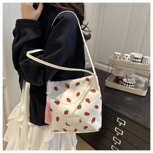 Detail van een witte bucket bag met aardbeienprint en roze fluwelen kwastje