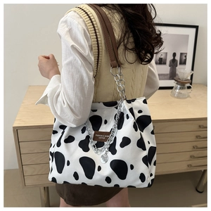 Detail of cow print tote bag featuring leather straps and silver metal chain decoration