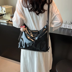 Black glossy tote shoulder bag for women featuring a plush bear charm in a cafe setting