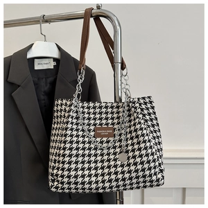 Detail of houndstooth tote bag featuring brown leather handles and silver chain accents