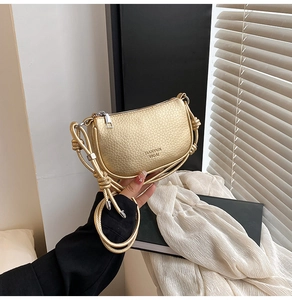 Détail d'un sac demi-lune doré texture galet avec poignée nouée et zip argenté