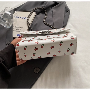 Détail du sac à bandoulière en cuir blanc avec imprimés cerises et bandoulière chaîne