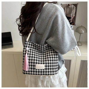 Detail van schoudertas met zwart-wit pied-de-poule patroon en roze kwastjes hanger