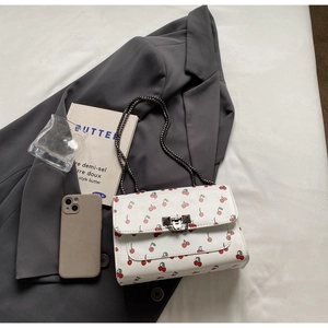Détail d'un sac carré blanc à motif cerise avec chaîne sur une veste grise