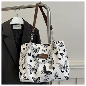 Detail of white tote bag with black butterfly prints, leather straps and metal chain