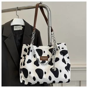 Close-up of cow print tote bag with brown leather handles and silver chain detail