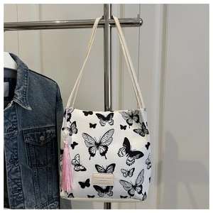Detail van witte canvas bucket-tas met vlinderprint en roze kwastje als decoratie