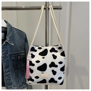 Detail van een tote bag met koeienprint en roze kwastje aan een stalen hanger