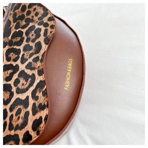Macro detail of leopard print flap and gold FASHION & BAGS text on brown leather saddle bag
