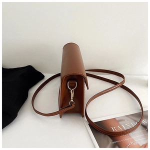 Detail view of the brown leather square bag showing stitching and metal D-ring attachment