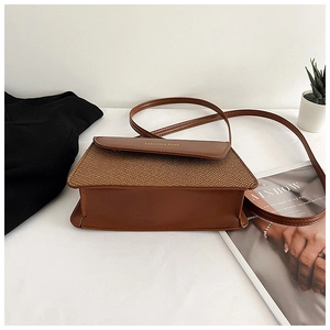 Detail of a brown crossbody bag with woven texture lid and golden fashion lettering