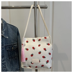 Detail van witte PU-leren emmertas met aardbeienprint en roze kwastjesaccessoire