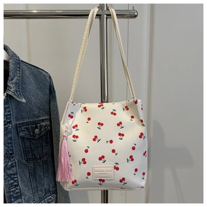 Detail van de witte draagtas met kersenprint, roze kwastje en leren merklabel