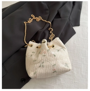 Détail de la broderie florale et texture tissée du sac seau crème avec chaîne dorée