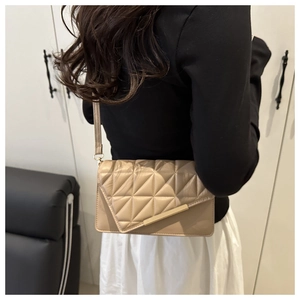 Detail view of beige crossbody bag with geometric quilting and gold hardware on model