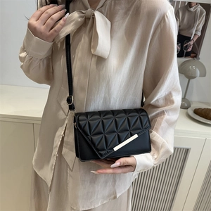 Elegant black quilted crossbody bag with triangle stitching and gold bar detail on model