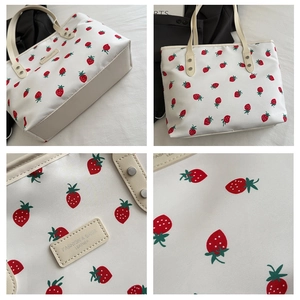 Close-up detail of white tote bag with red strawberry print and leather handles