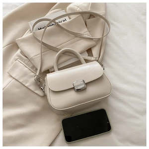 Close-up of cream leather handbag with silver clasp on beige blazer and book prop