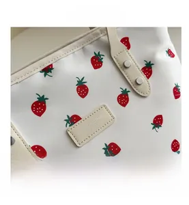 Close-up of strawberry print tote bag featuring leather label and metallic rivets