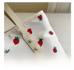 Detail of strawberry print tote bag with reinforced leather handles and rivet stitching