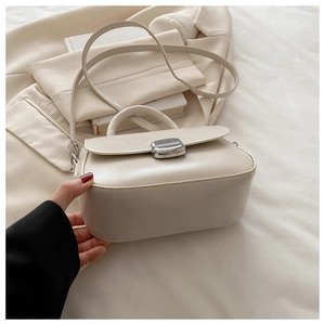 Detail of cream crossbody bag with silver metal lock on a neutral suit background