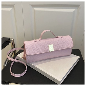 Close-up of pink woven crossbody bag with metallic lock resting on a decorative book