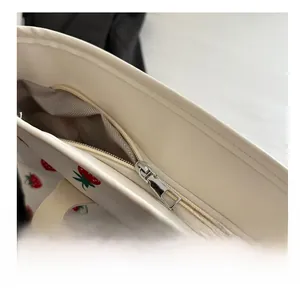 Detail of silver zipper and gray herringbone lining on a cream strawberry tote bag