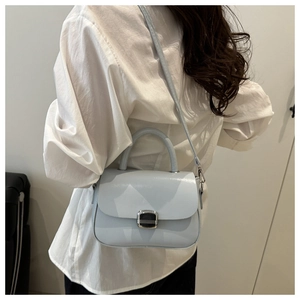 Detail of light blue crossbody bag with silver buckle worn by model against a white wall