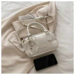 Détail du sac oreiller en PU crème avec nœud perlé, breloque cœur et bandoulière