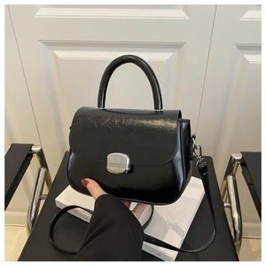 Detail of glossy black patent leather handbag with silver metallic buckle and top handle