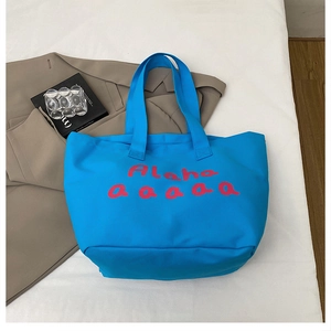 Detail of blue canvas tote bag featuring large red lettering and spacious interior design